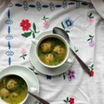 Bröselknödel in Suppentassen mit gebundener Gemüsesuppe auf Blümchentischtuch.