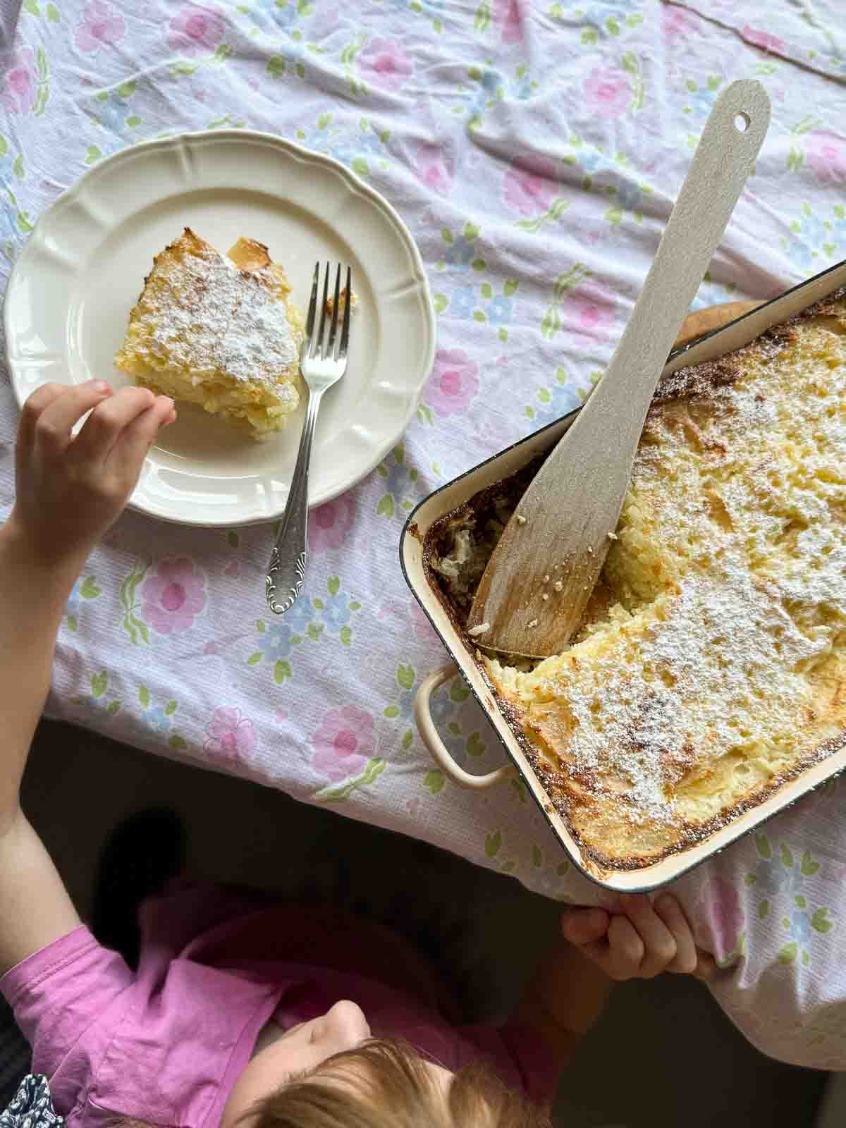 Grandma's baked rice pudding, sliced in a casserole dish, with a child snacking from it.