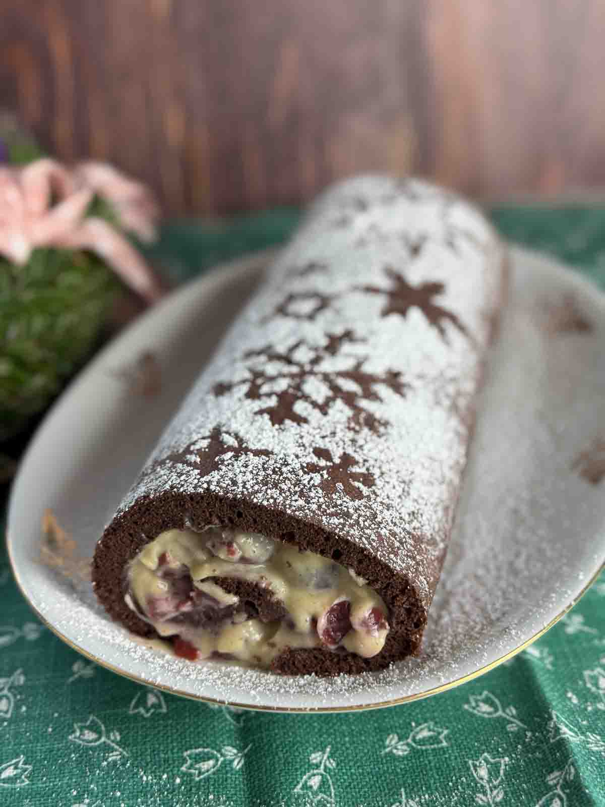 Dunkle Biskuitroulade mit Schneestern-Verzierung aus Puderzucker.